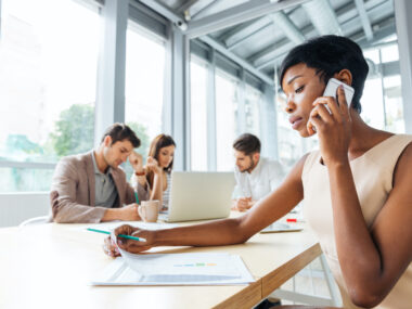 Focused young business woman working while talking on a cell phone in a meeting setting.